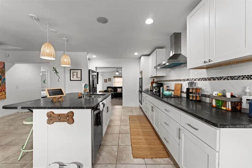 Modern kitchen with black countertops and white cabinetry featuring a spacious island and pendant lighting.