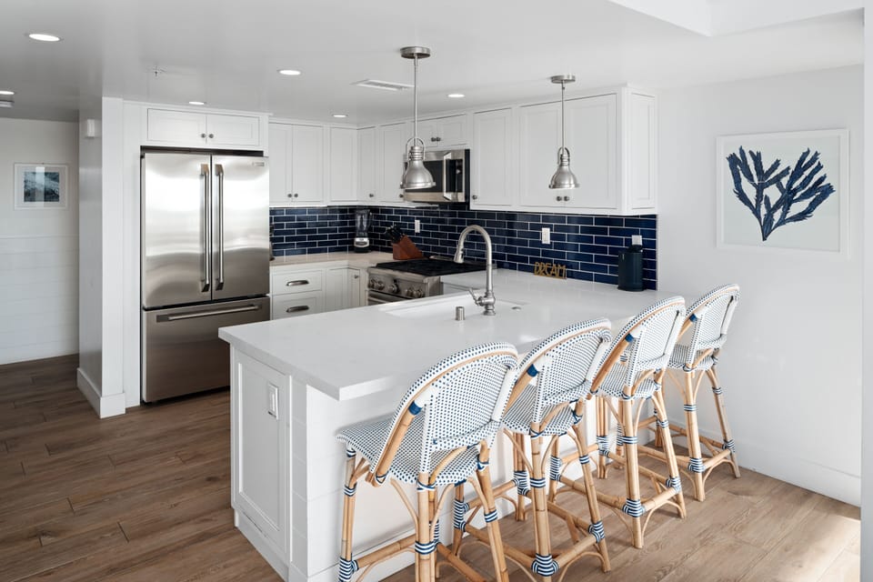 A luminous, modern-style open-plan kitchen featuring elegant sea tones, high-end appliances, and quality cookware, tableware, and utensils.