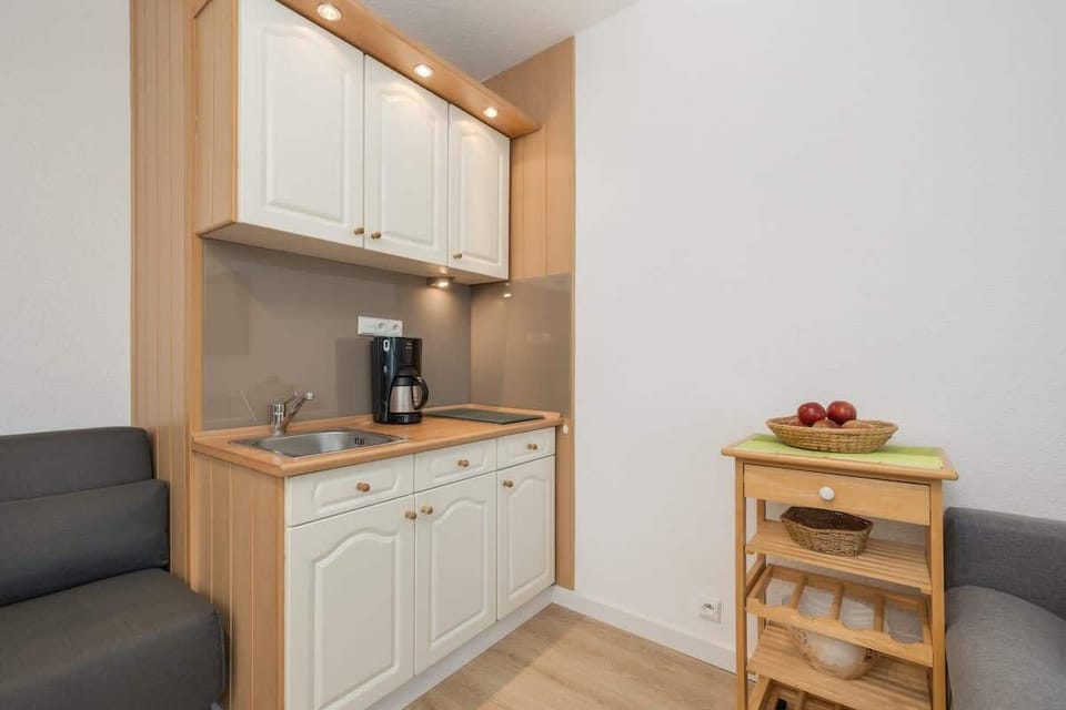 A kitchenette with white cabinets, a coffee machine, and a wooden shelf for extra storage.
