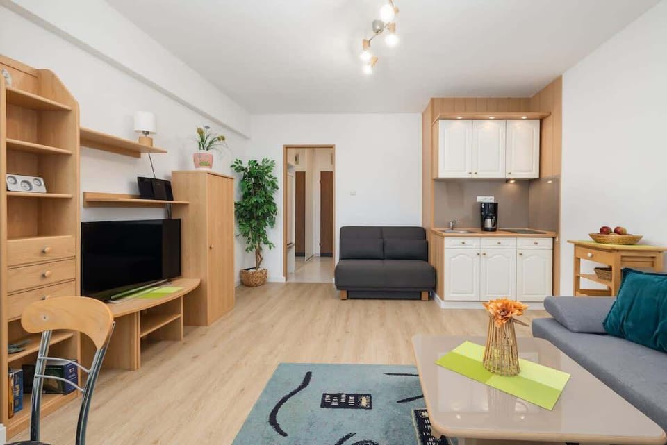 A view of the living area with a TV, shelving units, and an open, airy design with light wooden floors.
