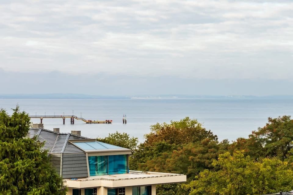 A scenic view from the balcony, showcasing nearby rooftops, greenery, and the ocean in the distance.
