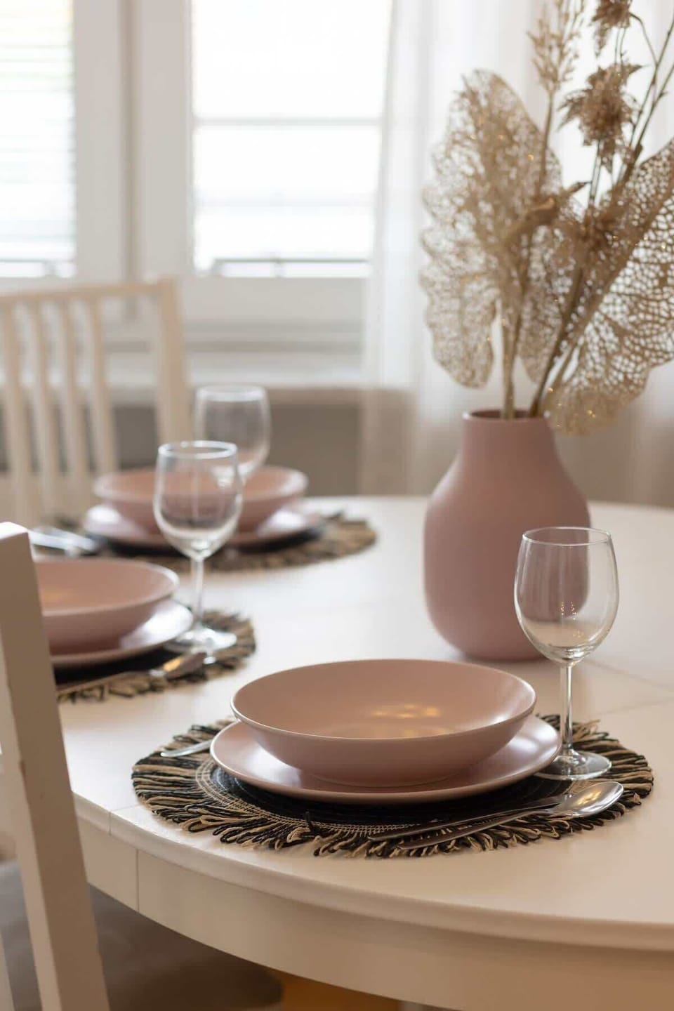An elegant dining area featuring a sleek white dining table set with minimalist décor, complemented by wooden flooring and soft, neutral tones.