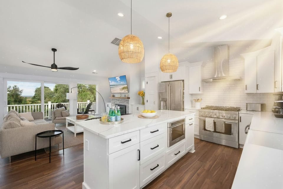 Step into this airy, open-plan haven where a sleek kitchen with modern appliances and a spacious island flows seamlessly into a cozy living area. Bathed in natural light, the room features a smart TV, ceiling fan, and panoramic views