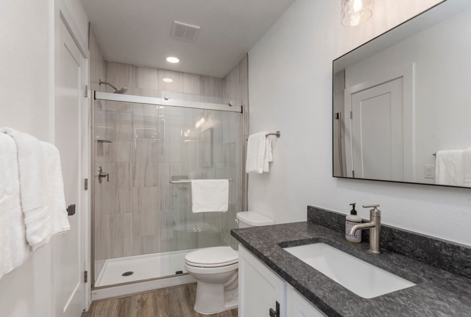 Step into your pristine en-suite bathroom, featuring a spacious walk-in shower, elegant granite countertops, and crisp white towels awaiting your arrival.