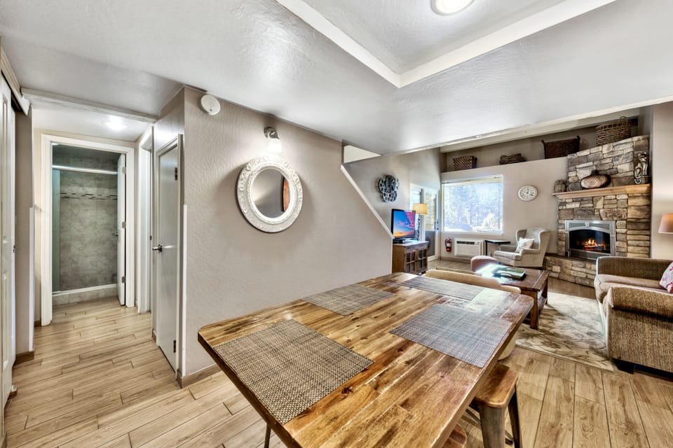 Your open-plan living space welcomes you with warm wood floors, a cozy stone fireplace, and rustic dining table perfect for mountain getaway meals.