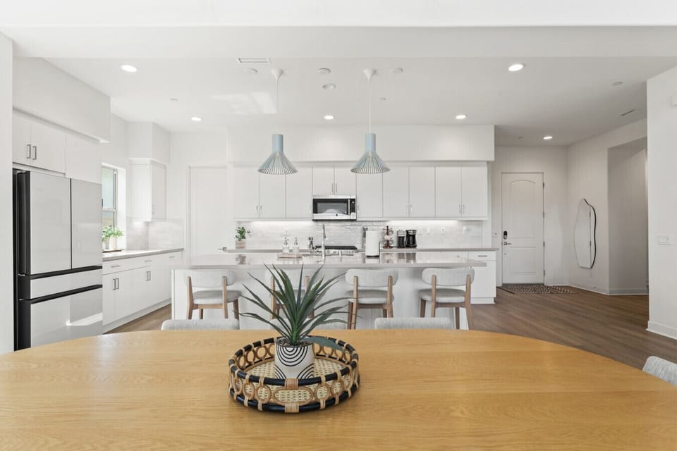 Sleek white kitchen w/ island seating, stainless appliances & pendant lighting.