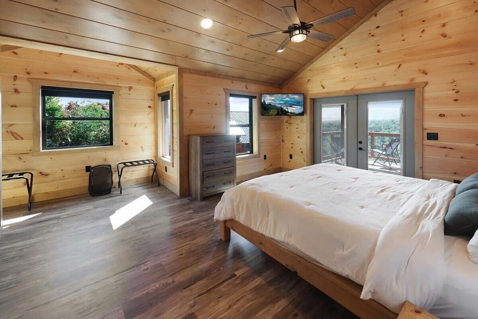 Spacious bedroom with wood-paneled walls and balcony access overlooking the forest.