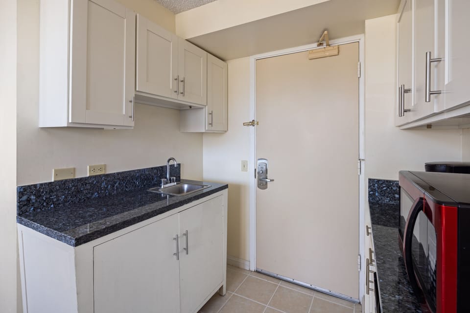 Your compact kitchen features sleek white cabinetry, elegant granite countertops, and a stainless steel sink—everything you need to prepare light meals during your stay.