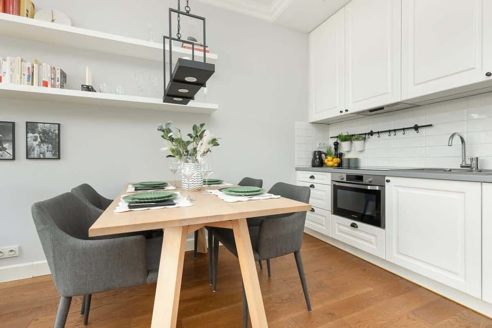A white kitchen setup with a wooden dining table, black countertops, and hanging shelves.
