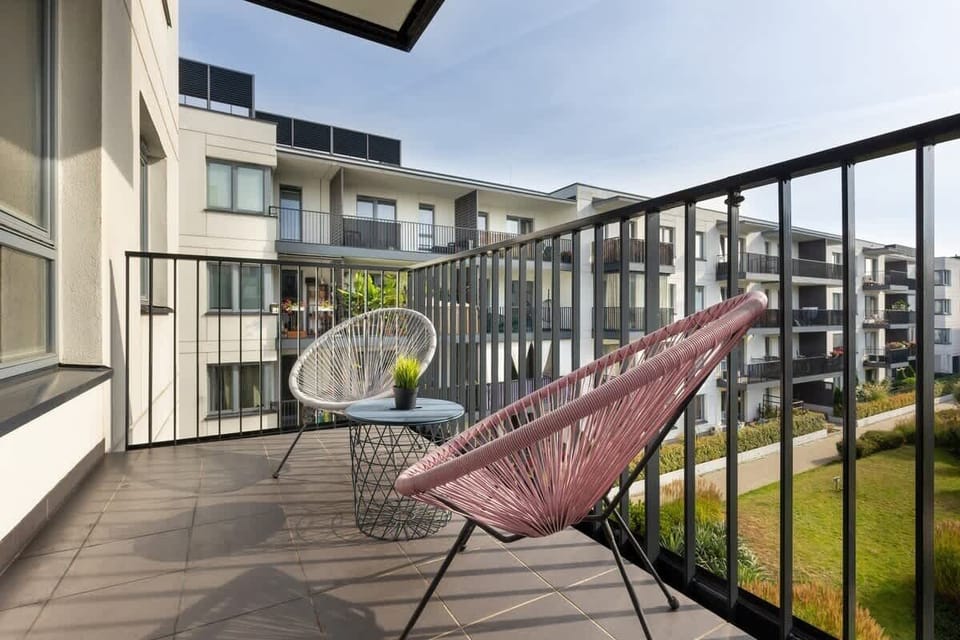 A balcony featuring pink wire lounge chairs overlooking a modern courtyard.
