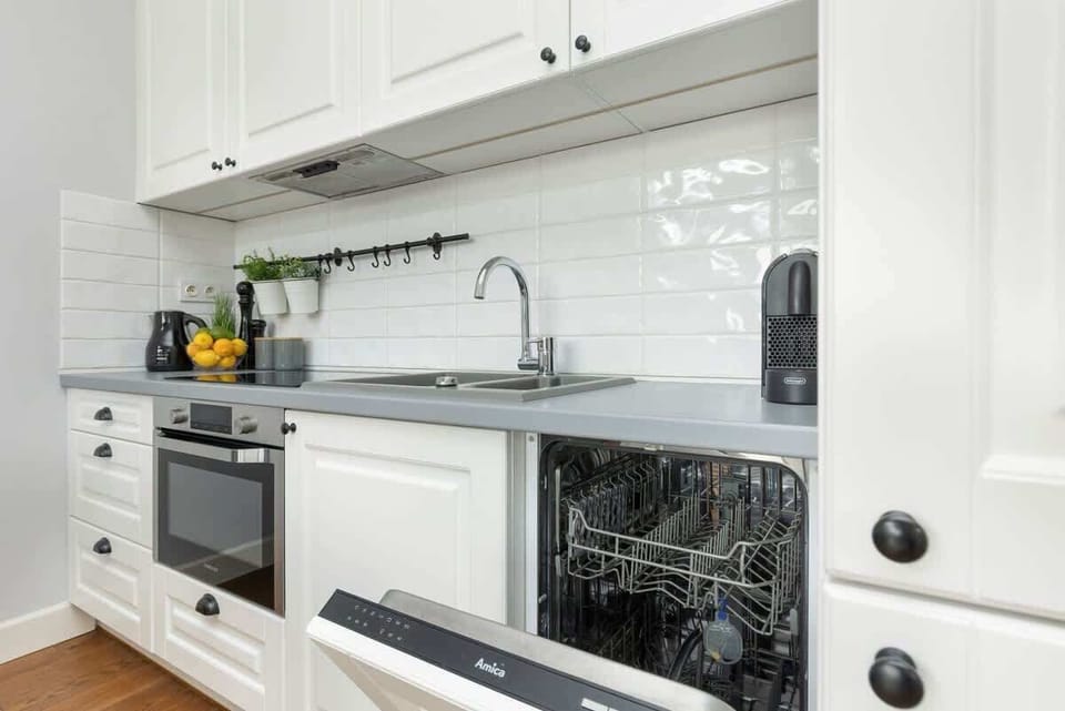 A partial view of the kitchen, showing white cabinetry, a dishwasher, and a glossy backsplash.






