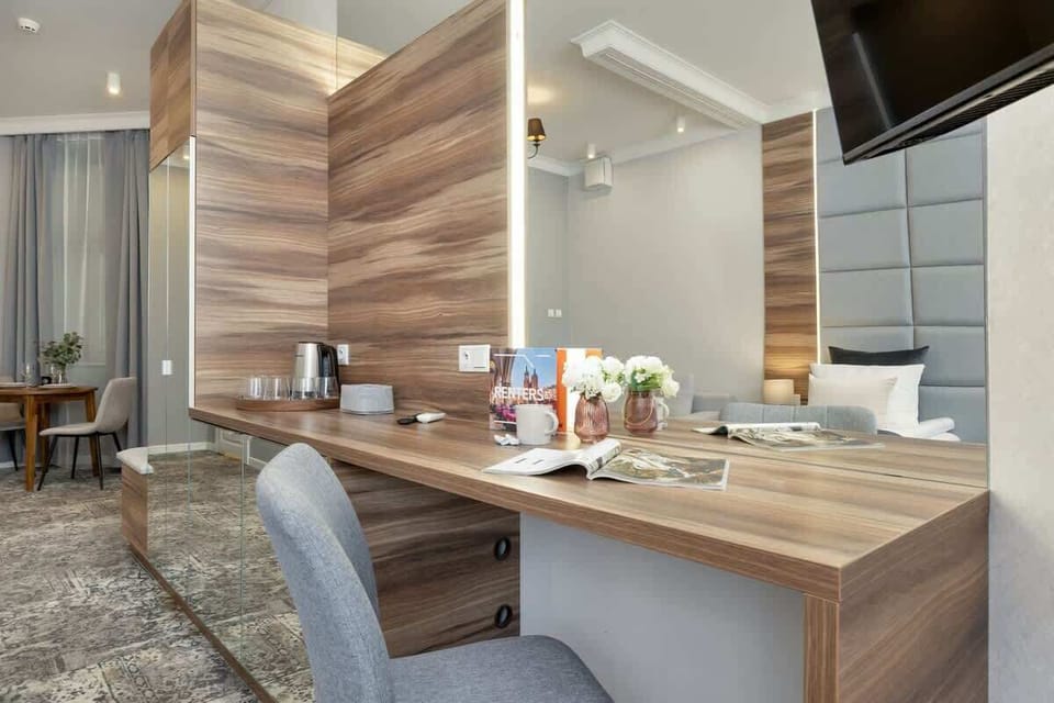 A wooden desk under a wall-mounted TV, with refreshments and a vertical panel behind it.
