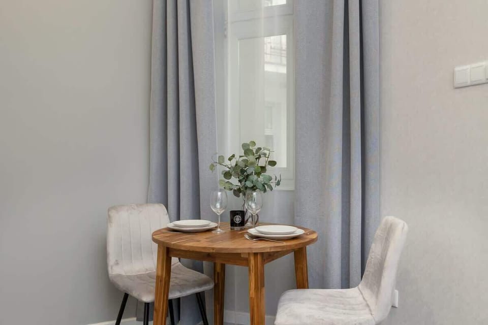 A small round table with two chairs, a potted plant in the center, and grey curtains in the background.
