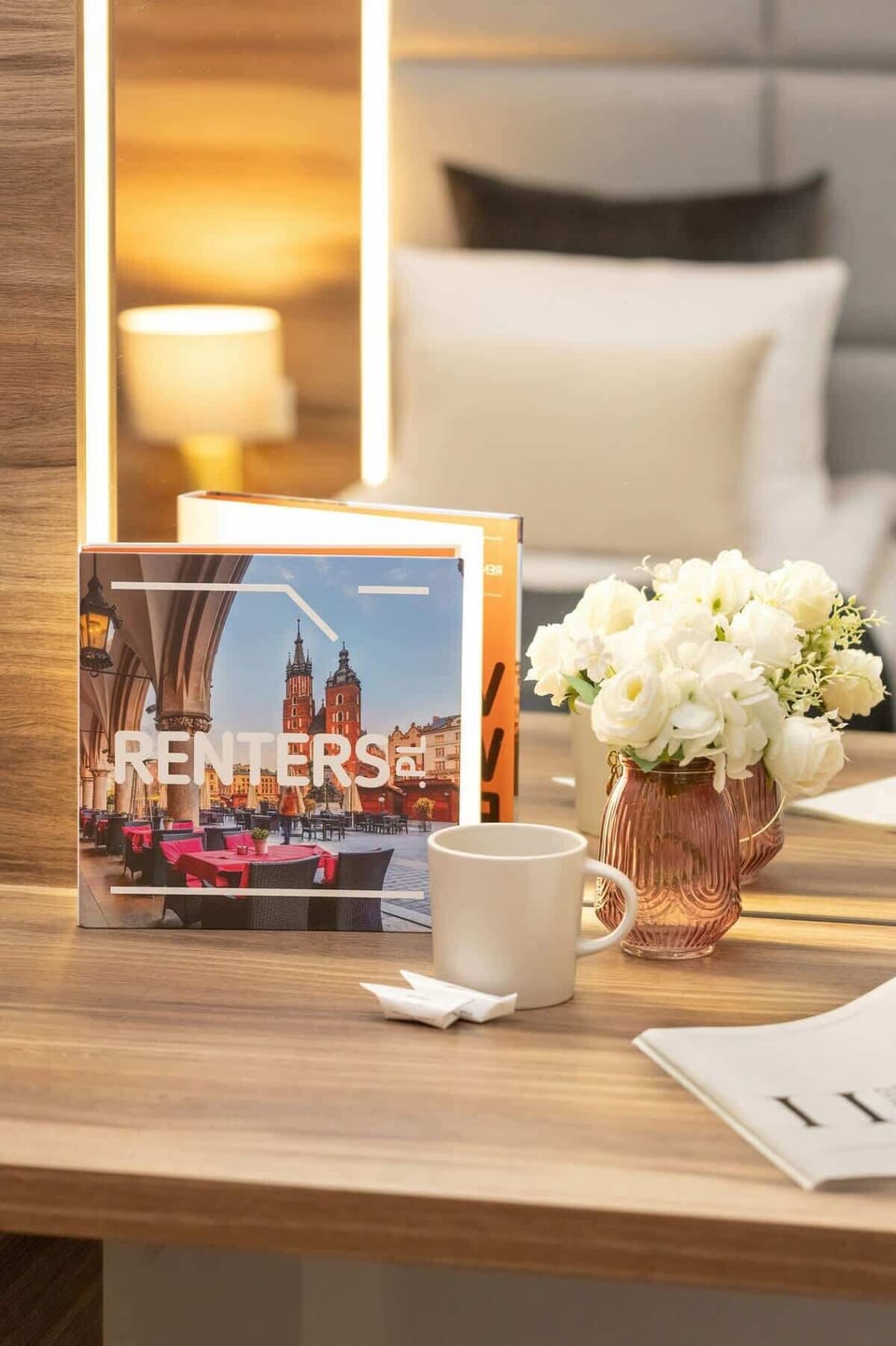 A small table with white flowers in a vase, a decorative brochure, and a lamp in the background.






