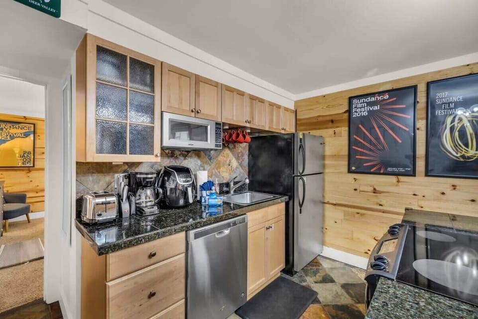 The kitchen is fully equipped with high-end stainless steel appliances, granite countertops, stone tile floors, and a stylish lighting fixture.