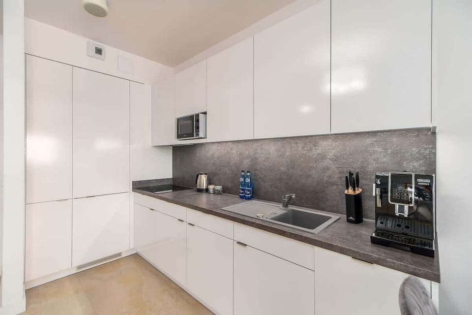 A modern kitchen with sleek white cabinets, a gray backsplash, and built-in appliances, designed for functionality and style.
