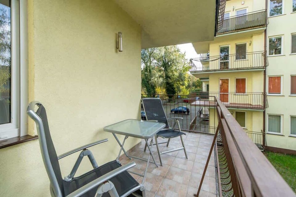 Another perspective of the balcony with a small table and chairs, overlooking greenery and nearby buildings.
