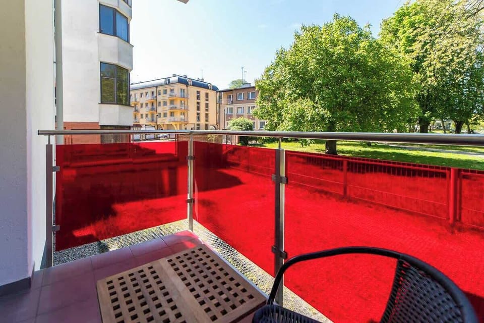 A close-up of the balcony with a red railing and outdoor seating, overlooking the greenery outside.
