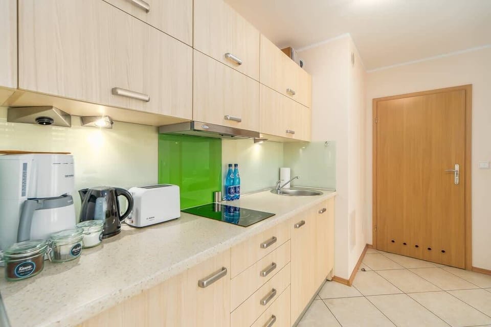A compact kitchen with white cabinets, a green backsplash, and modern appliances.

