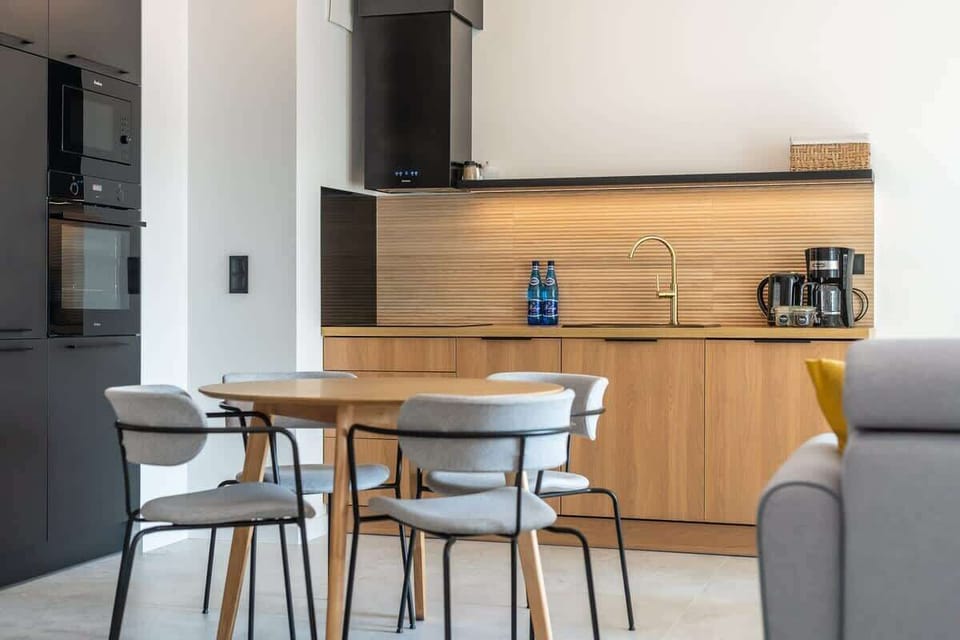 A small kitchen and dining space with a round table, set against modern black and wooden finishes.
