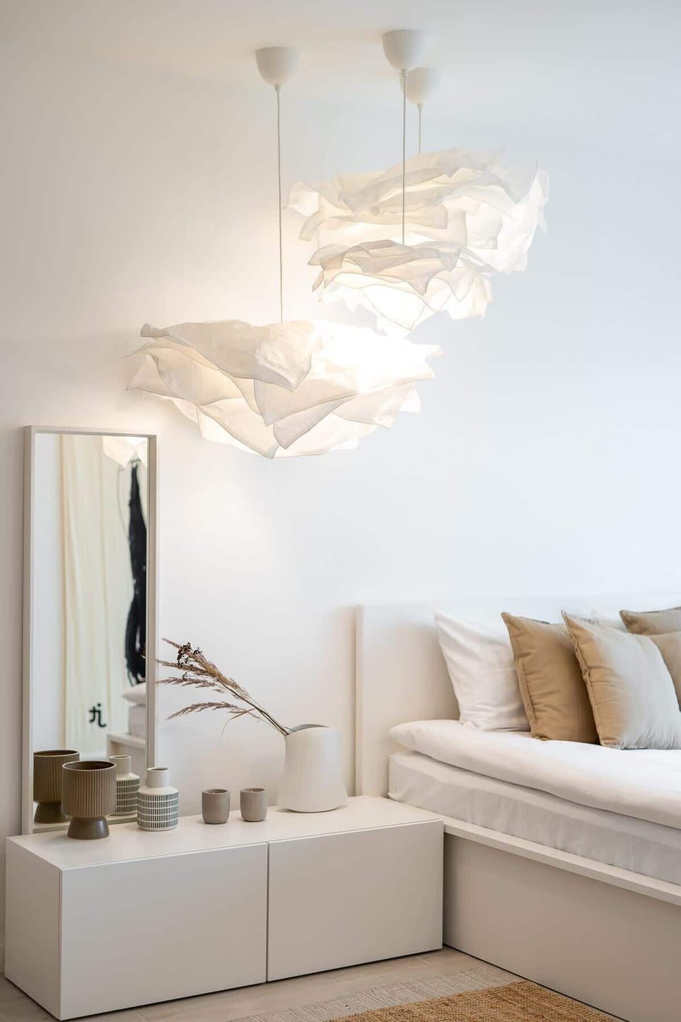 A bright bedroom with a large bed, soft bedding, and elegant lighting featuring unique pendant designs.
