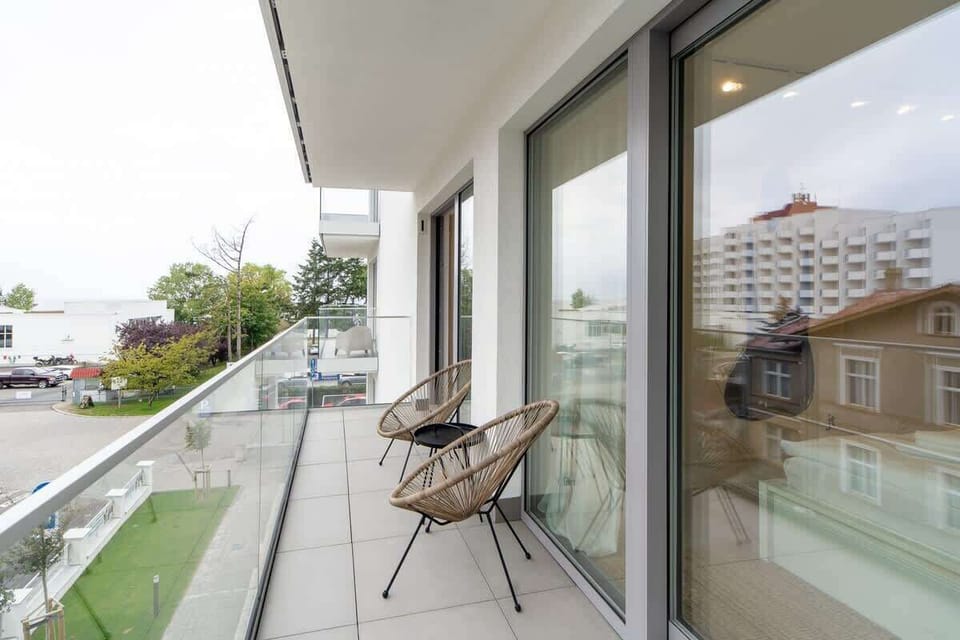A balcony with modern chairs and a small table, overlooking a serene neighborhood.
