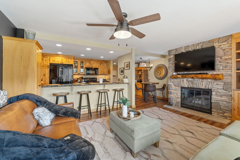 Unwind in your open-concept living space featuring warm wood finishes, a cozy stone fireplace, and modern kitchen perfect for gathering.