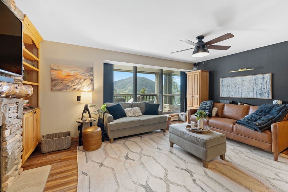 Unwind in your cozy living room with mountain views through expansive windows, comfortable leather seating, and rustic charm.