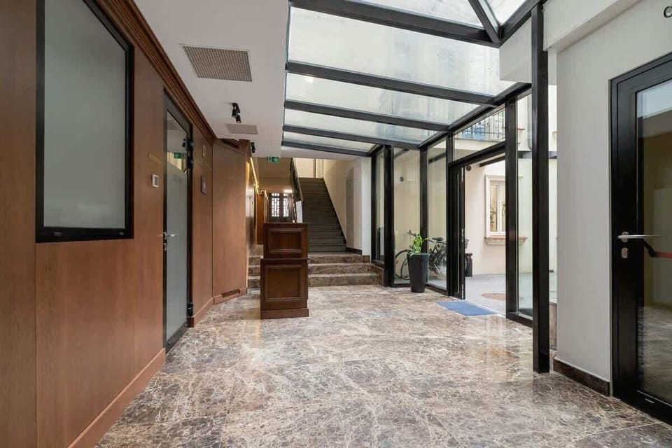 A spacious hallway with a glass ceiling, wooden wall panels, and a patterned carpeted floor.

