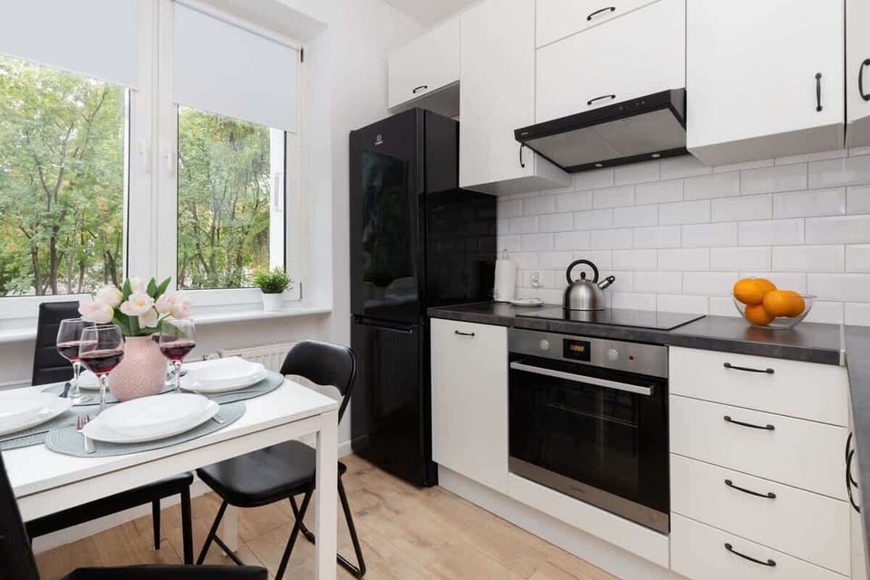 A modern kitchen with black-and-white cabinetry, a dining area, and a window letting in natural light.
