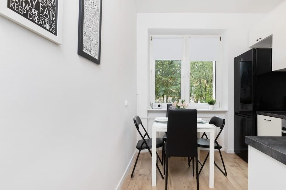 A dining area with a black table, white chairs, and a window overlooking greenery.
