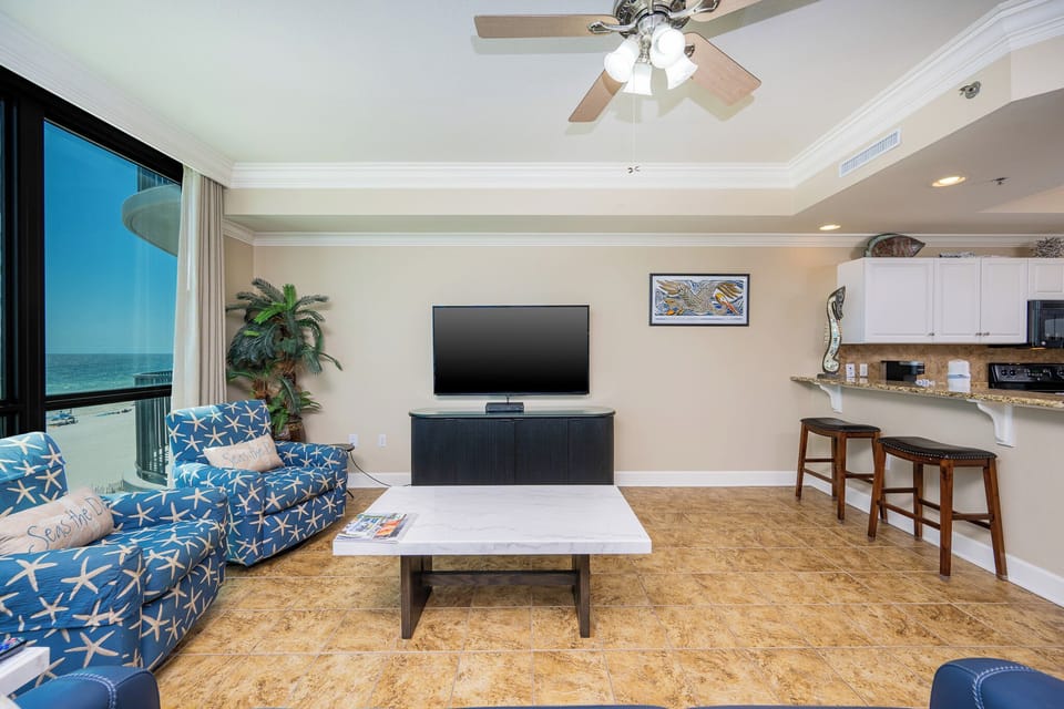 Vibrant seating area with starfish-patterned chairs, a large TV, and easy access to the kitchen bar