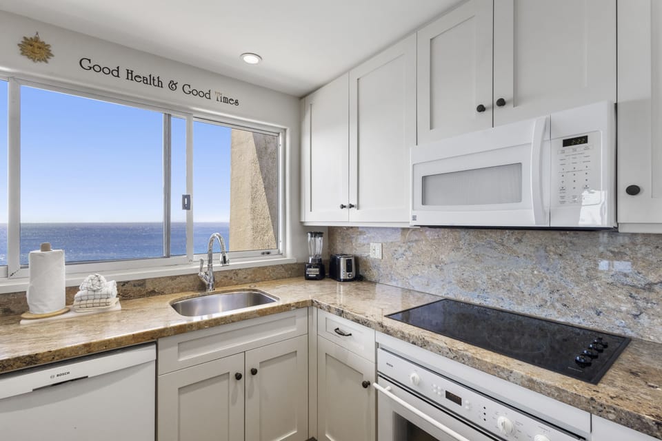 Picture yourself preparing morning coffee in this bright kitchen, where ocean views stretch endlessly beyond the window, turning every meal into a serene coastal experience.