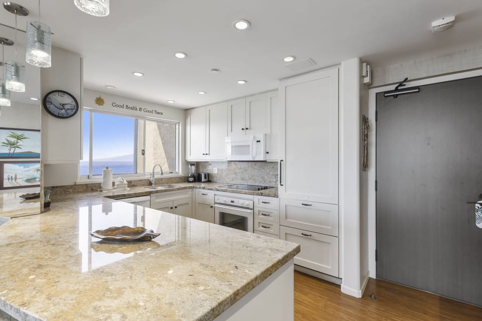 Your fully-equipped kitchen features stunning coastal views, gleaming granite countertops, and modern appliances—perfect for preparing fresh meals while enjoying ocean breezes through the window.