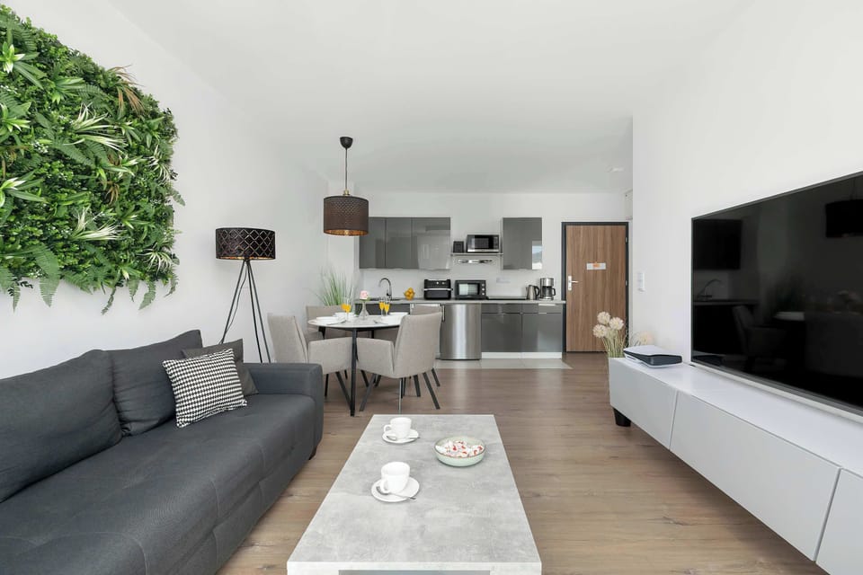 A modern living room with a gray sofa, white coffee table, and a large green wall decoration.