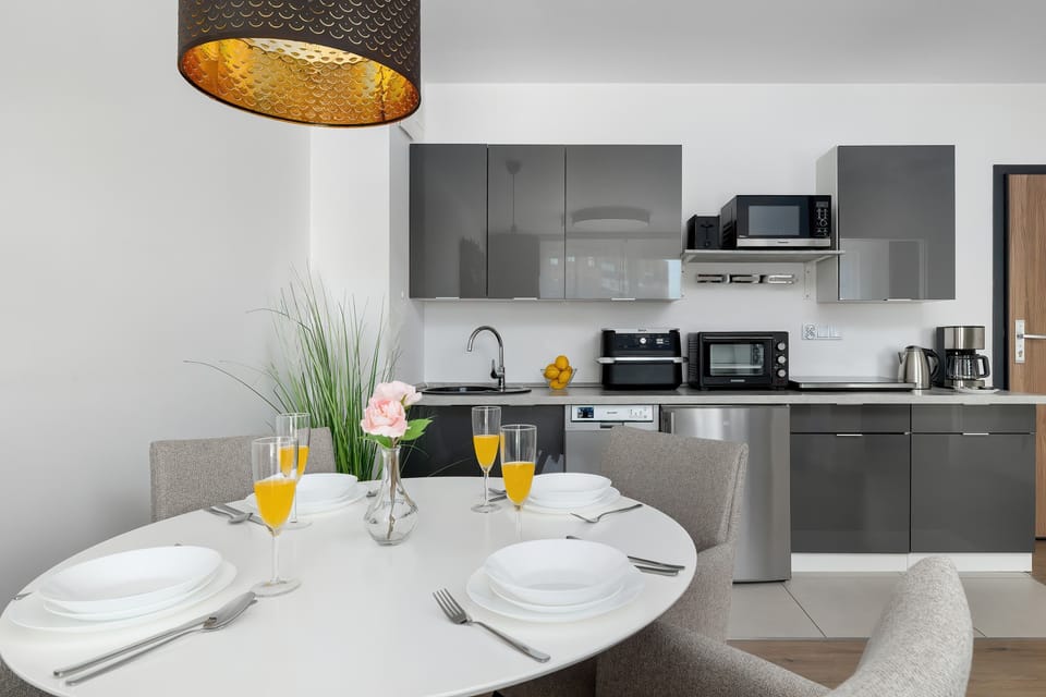 A dining area with a round table set for breakfast, next to a sleek, modern kitchen.