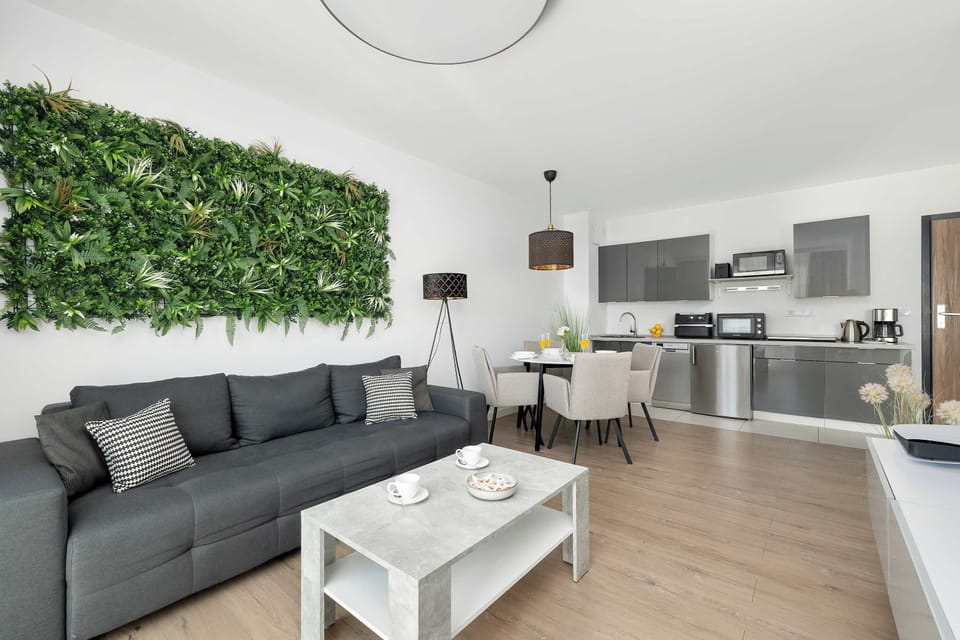 A modern living room with a gray sofa, white coffee table, and a large green wall decoration.