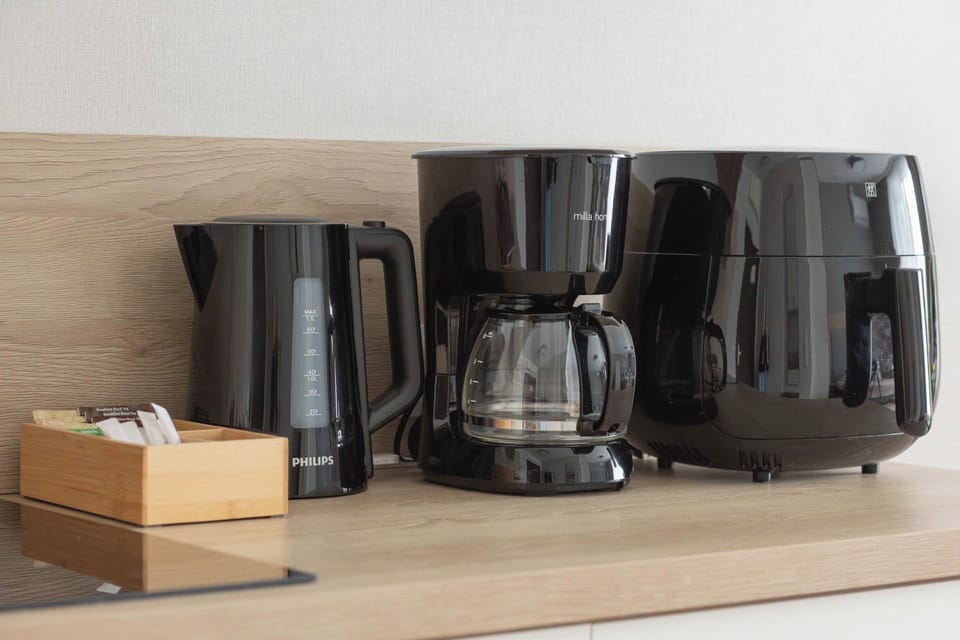 A coffee station with a black coffee machine, an electric kettle, and a small wooden box placed on a light countertop. The setup provides convenient access to hot drinks.