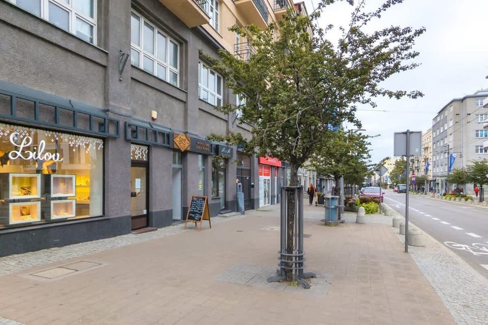 A wider street view with trees, modern architecture, and a pedestrian pathway.
