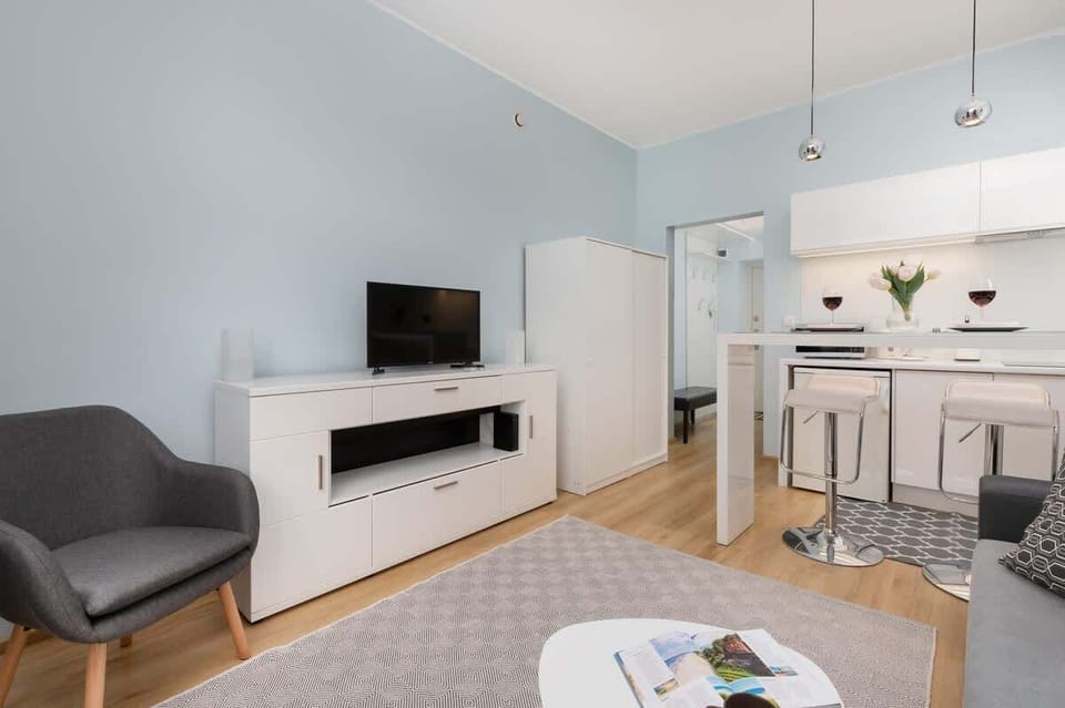 A cozy open-plan living area with a sofa, TV console, and kitchenette.
