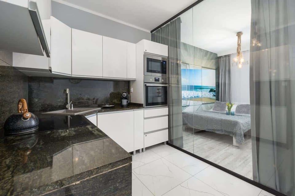 A wide view of the kitchen, showcasing its white cabinetry and black stone backsplash.
