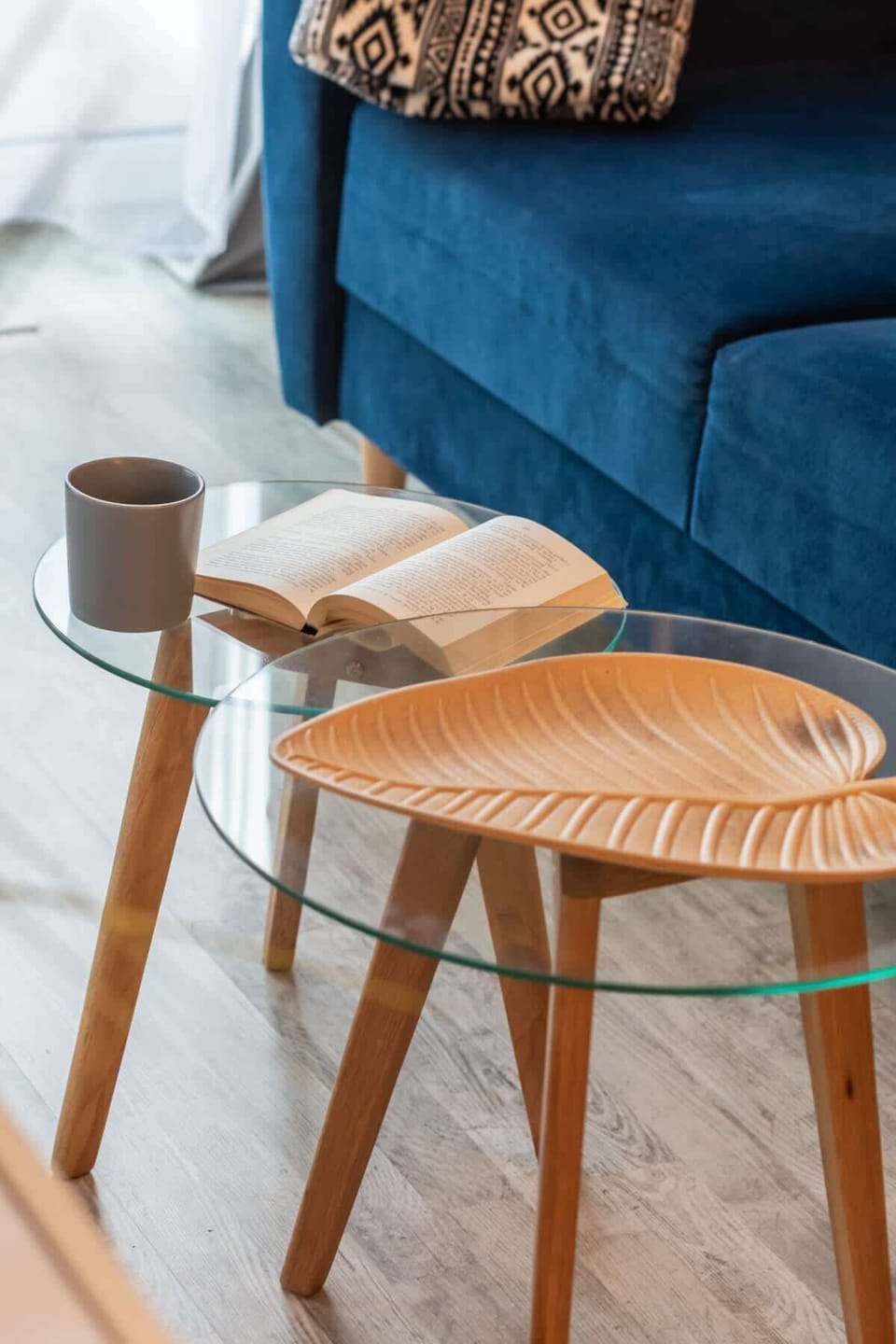 A close-up of a wooden stool with a modern design, placed near a blue sofa.
