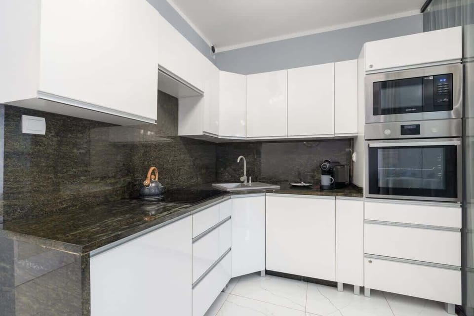 A sleek white kitchen with black countertops and integrated appliances.
