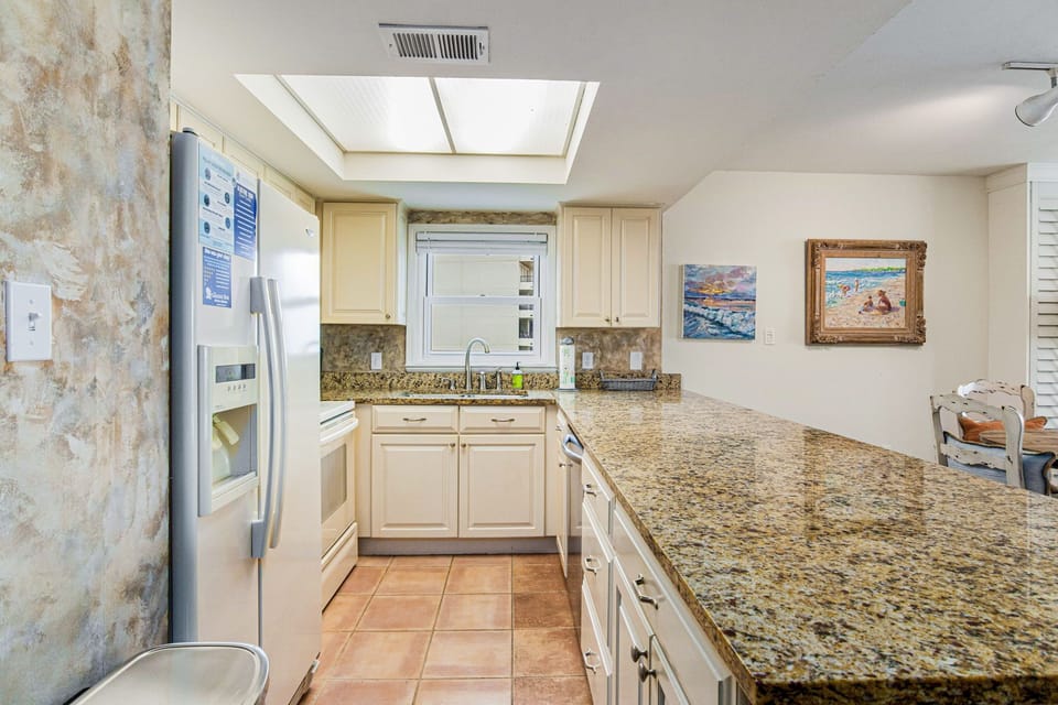 Lei Lani 401's kitchen featuring white cabinetry, granite countertops, and bright natural light — fully equipped for your Orange Beach vacation.