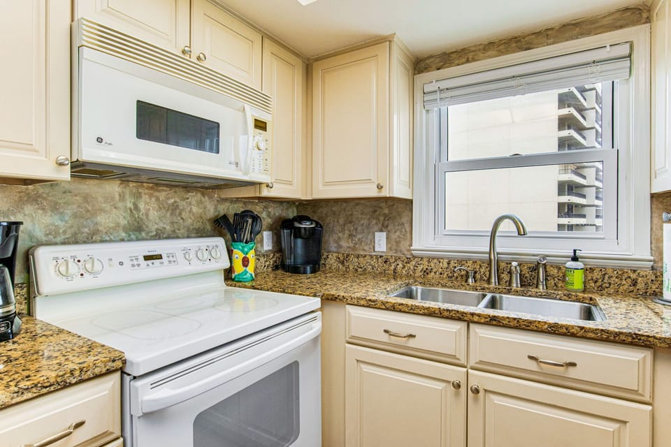 The fully equipped kitchen at Lei Lani 401, Orange Beach — white cabinets, granite countertops, range, microwave, and Keurig coffee maker ready for your stay.