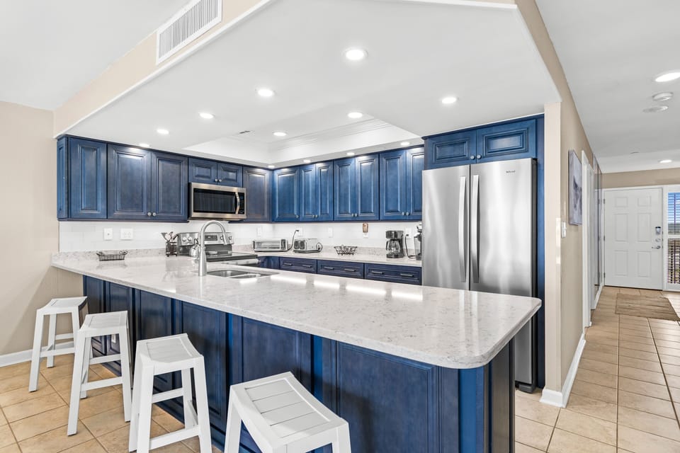 You'll love cooking in this spacious kitchen with rich navy cabinets, marble counters, and modern appliances—plus bar seating for casual meals.