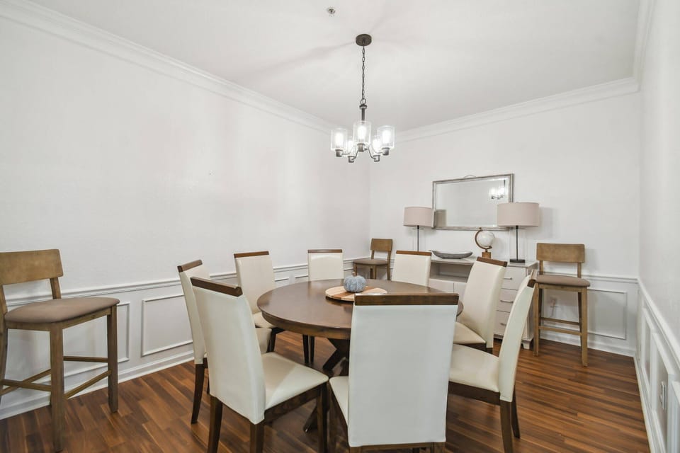 Enjoy an elegant dining area with a round wooden table and plush cream chairs, perfect for relaxed meals. A beautiful chandelier brightens the rich hardwood floors and stylish decor, creating a warm and inviting ambiance.