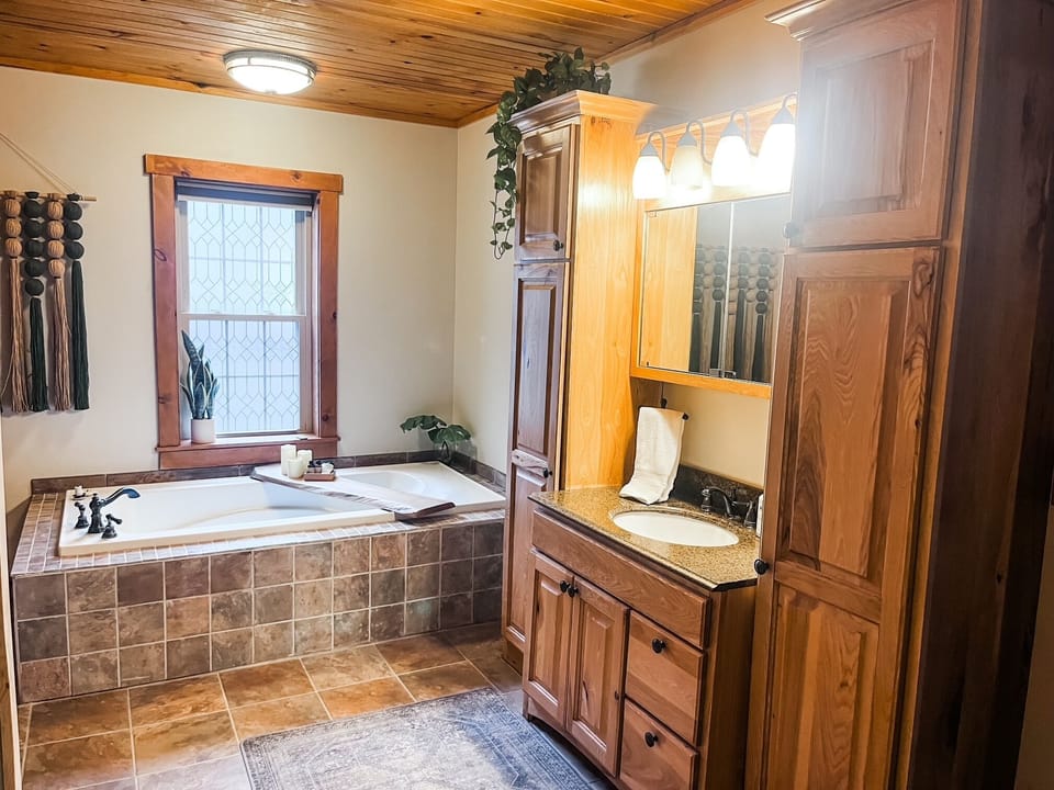 This spacious master bath offers all the comforts of home with a deep soaking tub, warm wood finishes, and plenty of counter space to settle in and unwind.