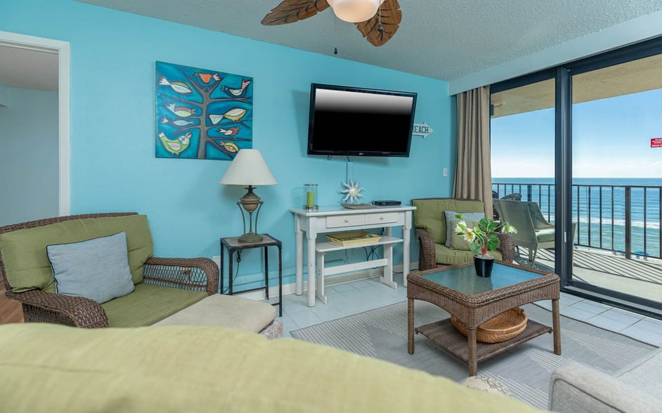 The inviting living area features a large TV, cozy seating, queen sofa-sleeper, and a beautiful view of the beach