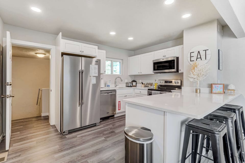 Bright kitchen with a white island and bar stools, stainless steel fridge, and warm wood flooring. Pull up a seat with your morning coffee or prep meals on the island while everything you need sits within easy reach.